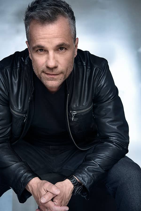 Le chanteur Bruno Pelletier assis sur un tabouret, portant les cheveux courts et un blouson de cuir noir.