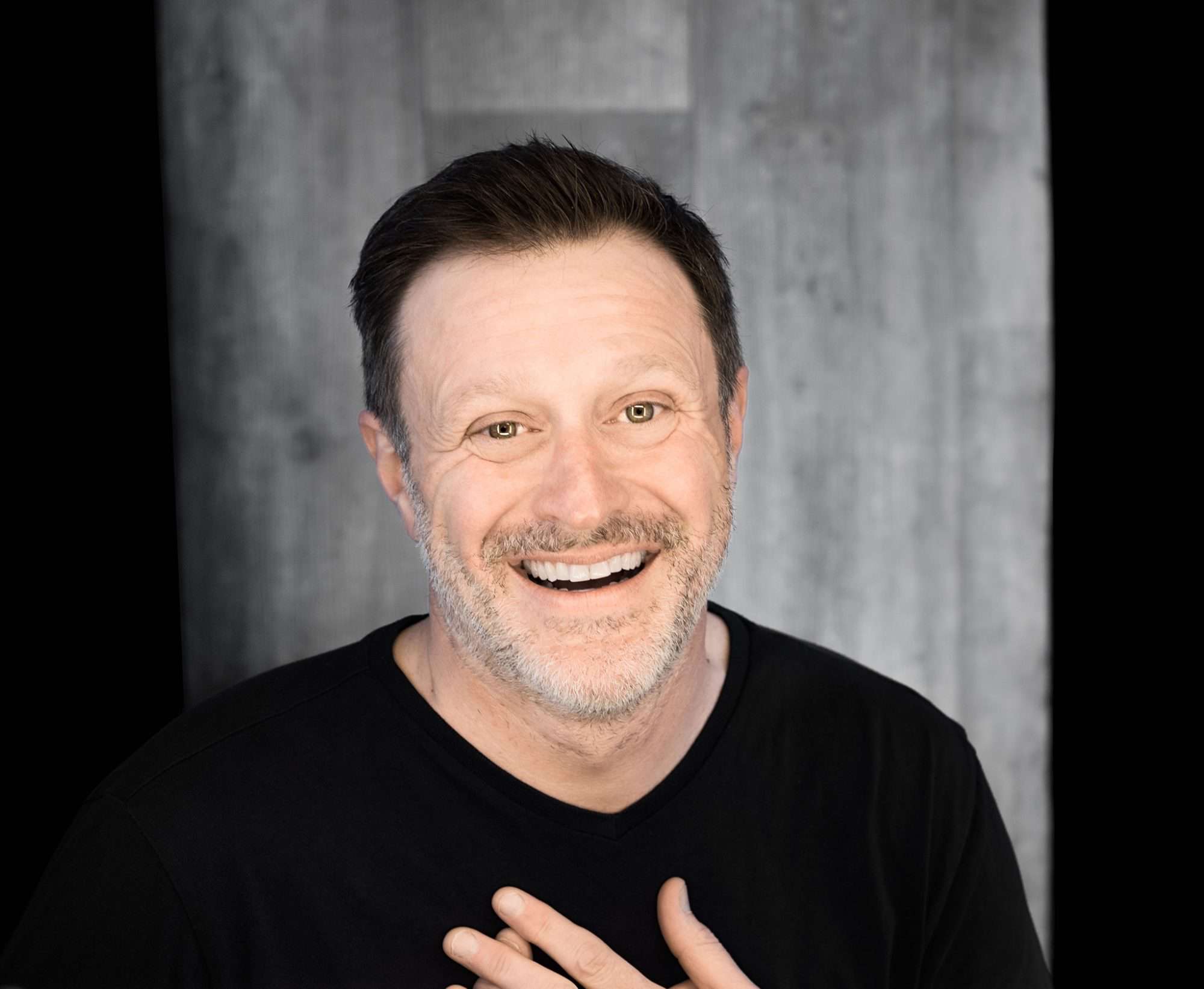 Stéphane Fallu humoriste souriant avec chandail noir.